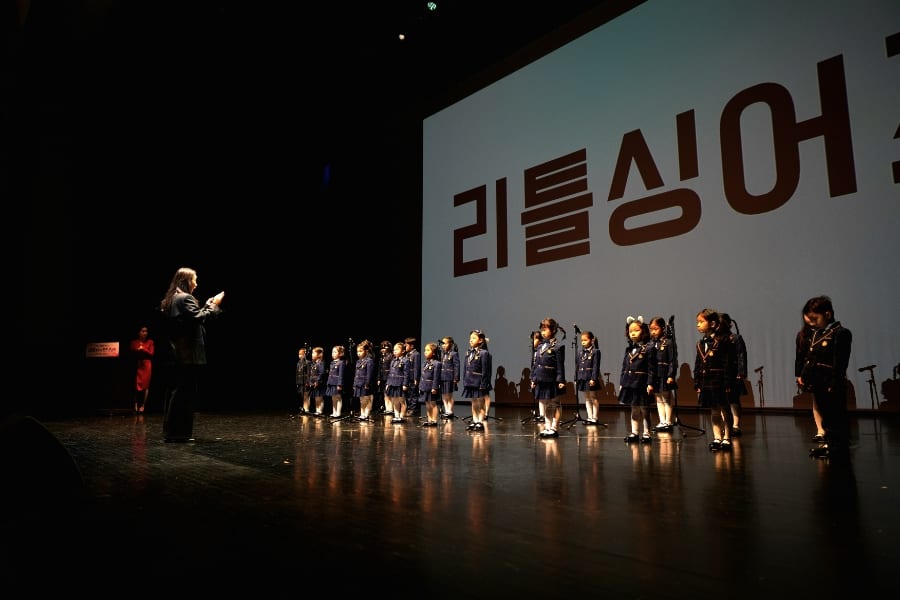 리틀싱어즈 화면 앞 무대에서 지휘에 맞춰 노래하는 선율반 단원들